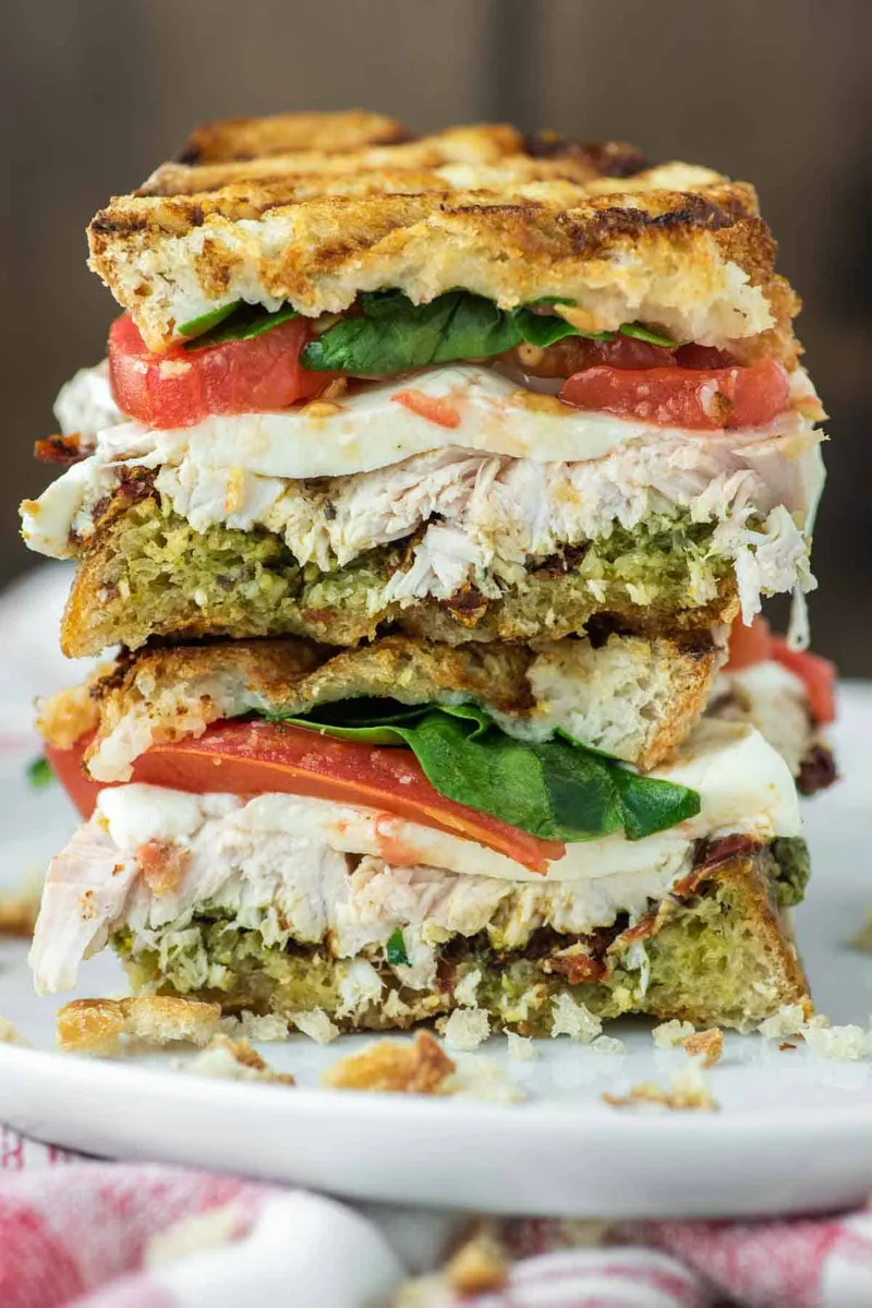 A pesto turkey sandwich on grilled sourdough, cut in half and stacked, with tomato, mozzarella and spinach showing between the layers