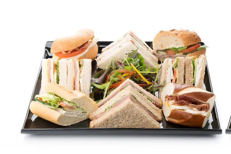 A black platter of half sandwiches on white, sourdough and baguette, with a dressed leaf salad in the middle